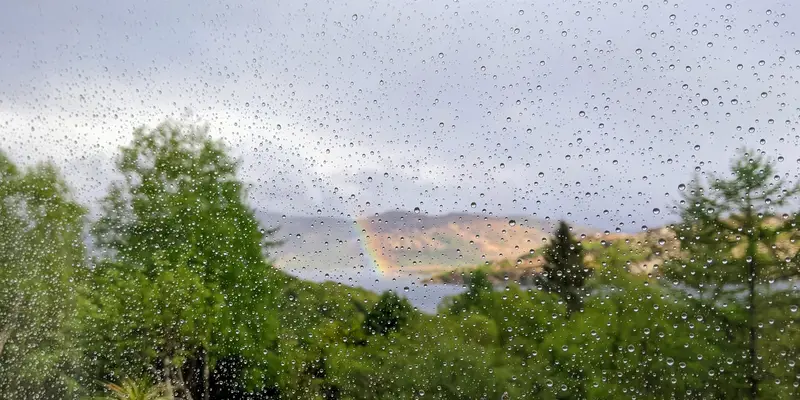 Photo of raindrops on a window with a rainbow in the background