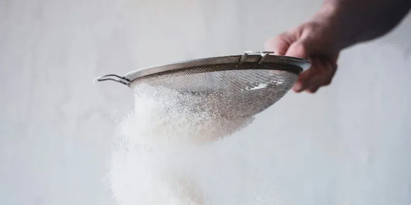 Someone holding a seive and shaking icing sugar throughn it