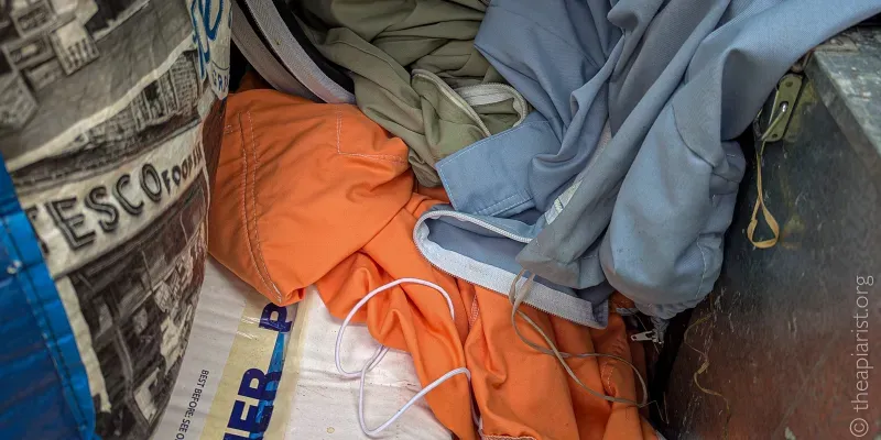 Photograph of three different cotton beesuits, orange, blue and tan, in the boot of a car