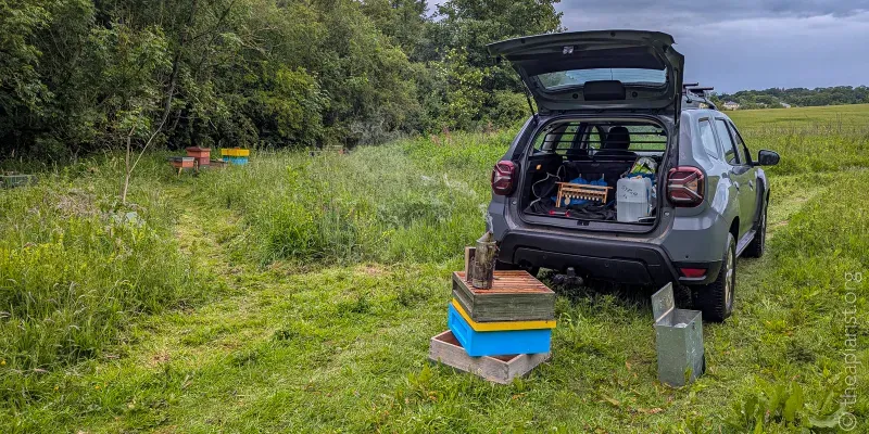 A car in a field with the boot open, showing that it is filled with beekeeping equipment