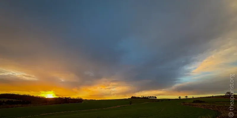A photograph of a sunrise, with the foreground in shadow, and the sky orange and purple