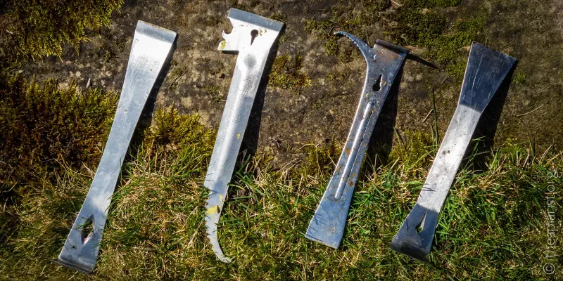 Four beekeeping hive tools lying in a row in the grass.