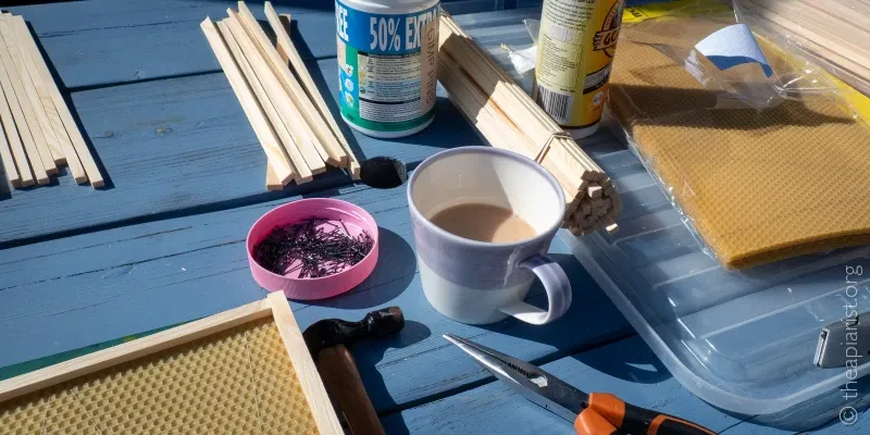 A picture of a cup of tea on an outdoor table, surrounded by items used to build frames for bee hives.