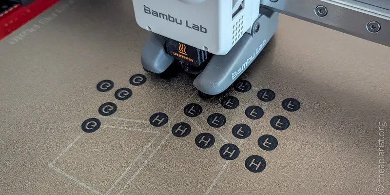 A picture of a 3D printer creating small black circles on a bronze plate, each circle has the inverse of a letter to identify it.