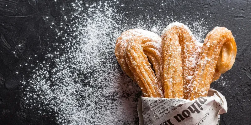 A newspaper wrap of churros with powdered sugar shaken over them