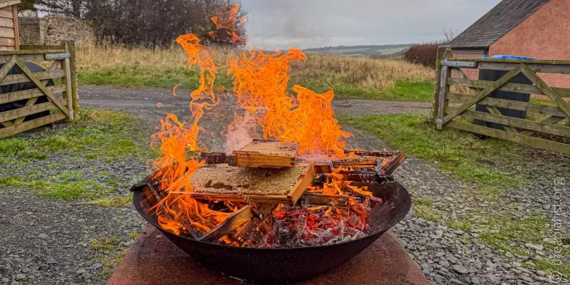 A circular metal fire pit filled with old frames from a beehive, burning fiercely.