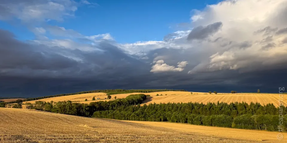 Recently harvested fields in the evening sunshine with dark thunderclouds on the horizon.