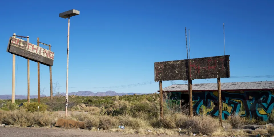 Old billboards in a desert setting with distant hills.